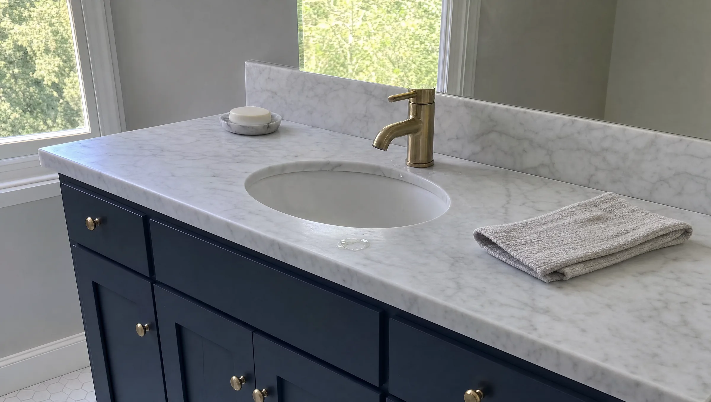 White marble vanity top with gray veining and an undermount sink with a brass faucet
