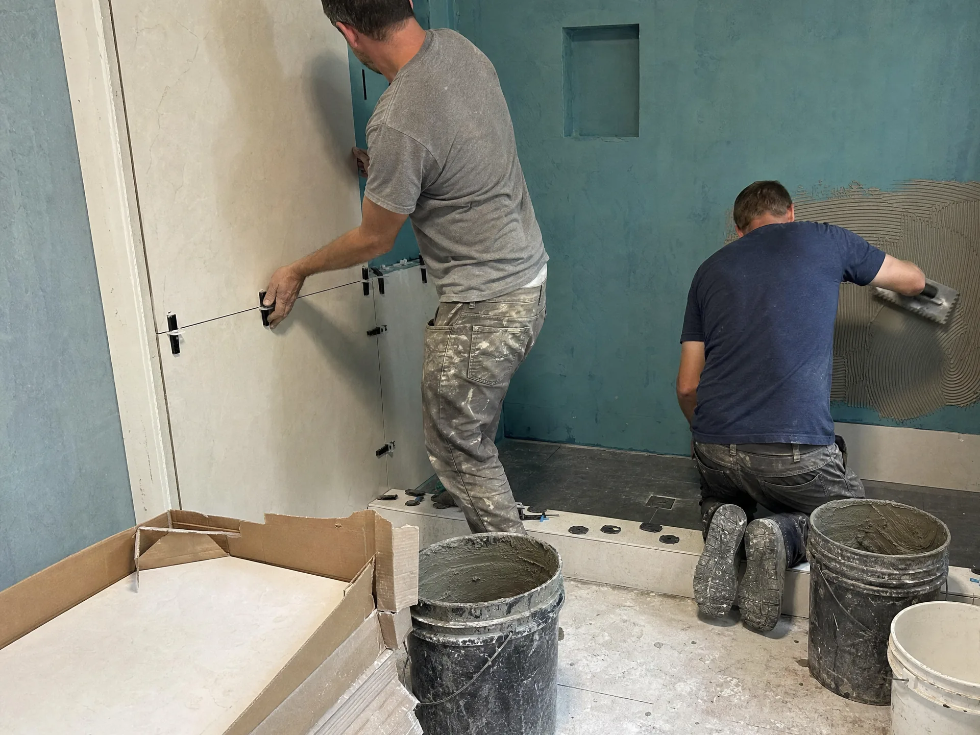 Tile setters installing large-format porcelain tile on a shower wall over a waterproofing membrane