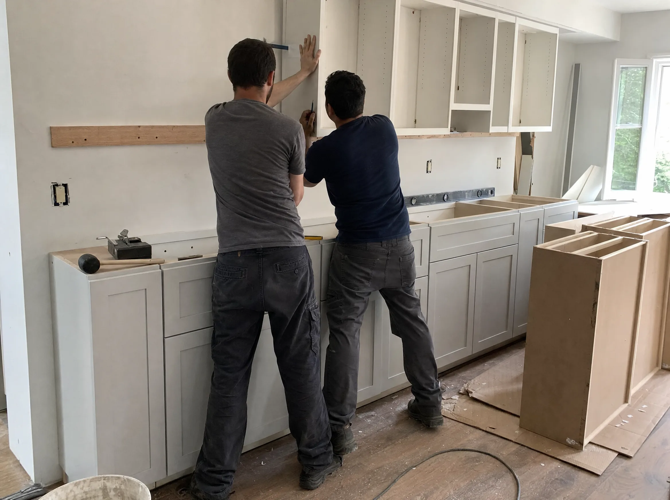 Cabinet installers fastening a new upper cabinet to the wall during a kitchen cabinet installation