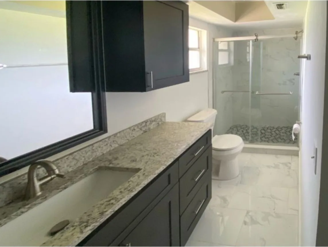 After: Bathroom after the remodel: dated vanity and shower replaced with a dark vanity, granite top and glass shower