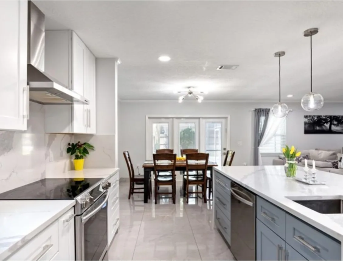 After: Kitchen after the remodel: oak cabinets and dark granite replaced with white cabinets, quartz counters and new lighting