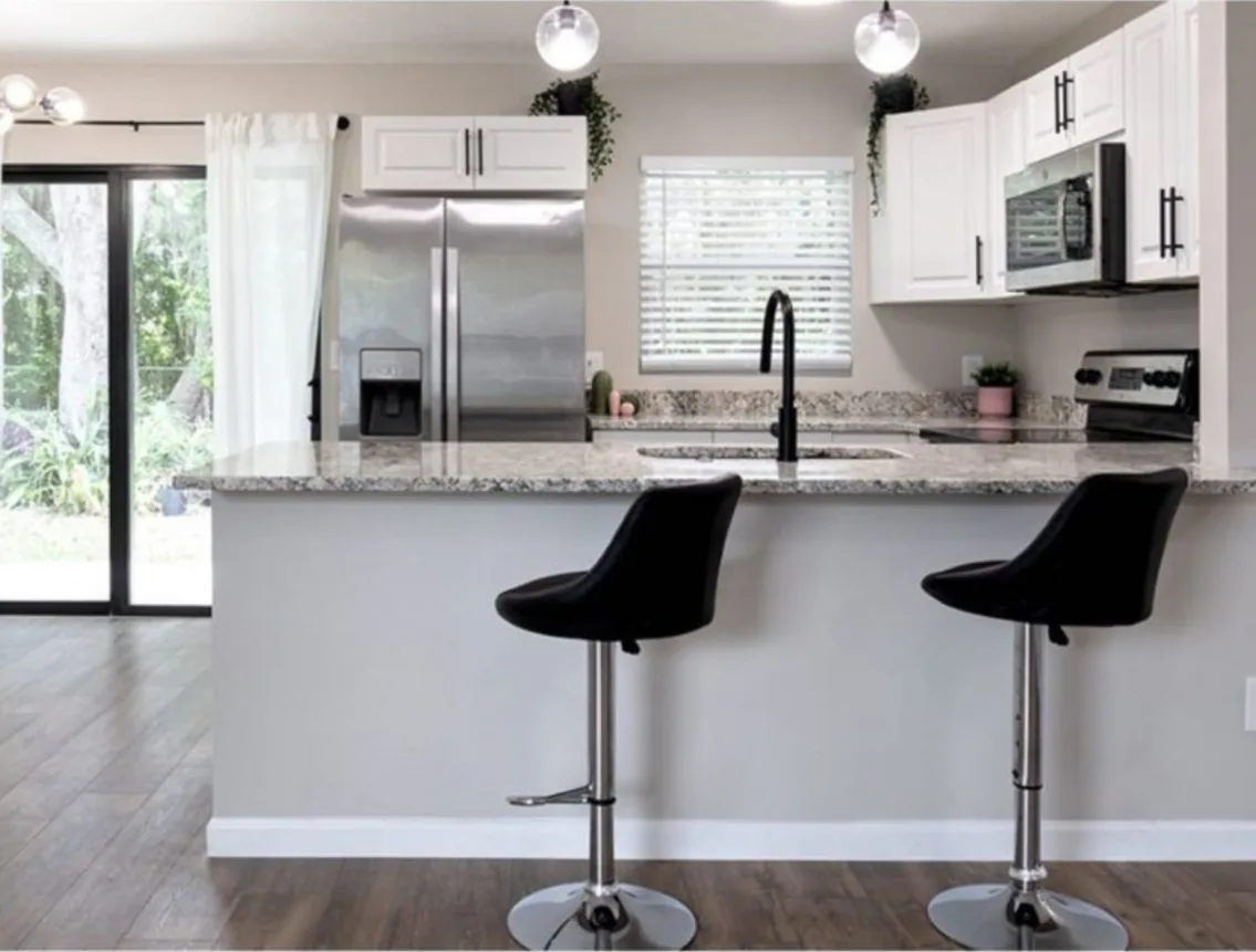 After: Kitchen after the remodel: cramped dated kitchen opened up with white cabinets and a granite island with bar stools