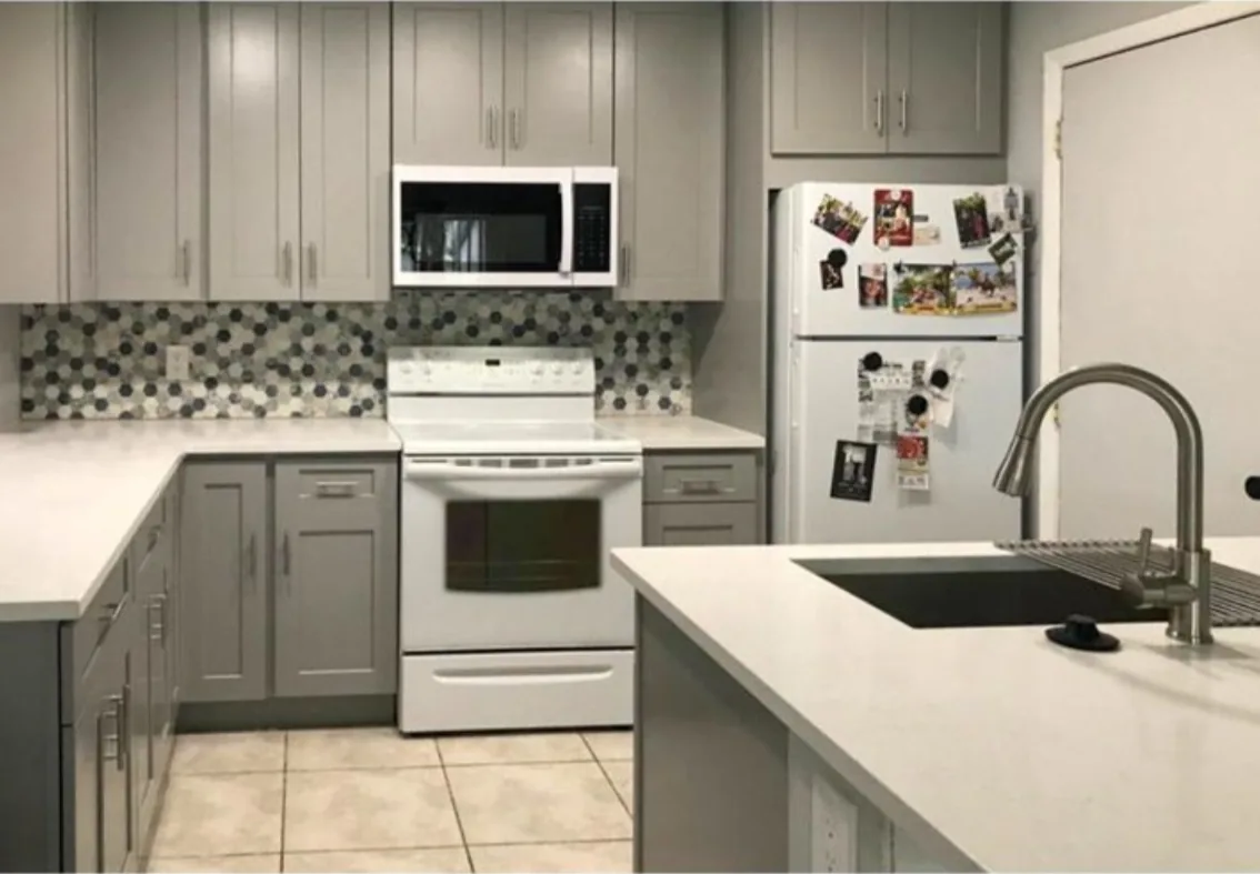 After: Kitchen after the remodel: dated white kitchen redone with gray shaker cabinets, quartz and mosaic backsplash
