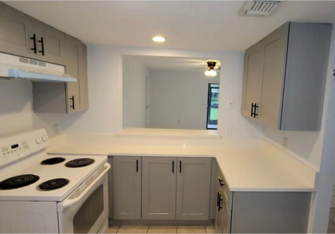After: Kitchen after the remodel: old laminate kitchen replaced with gray cabinets and quartz counters