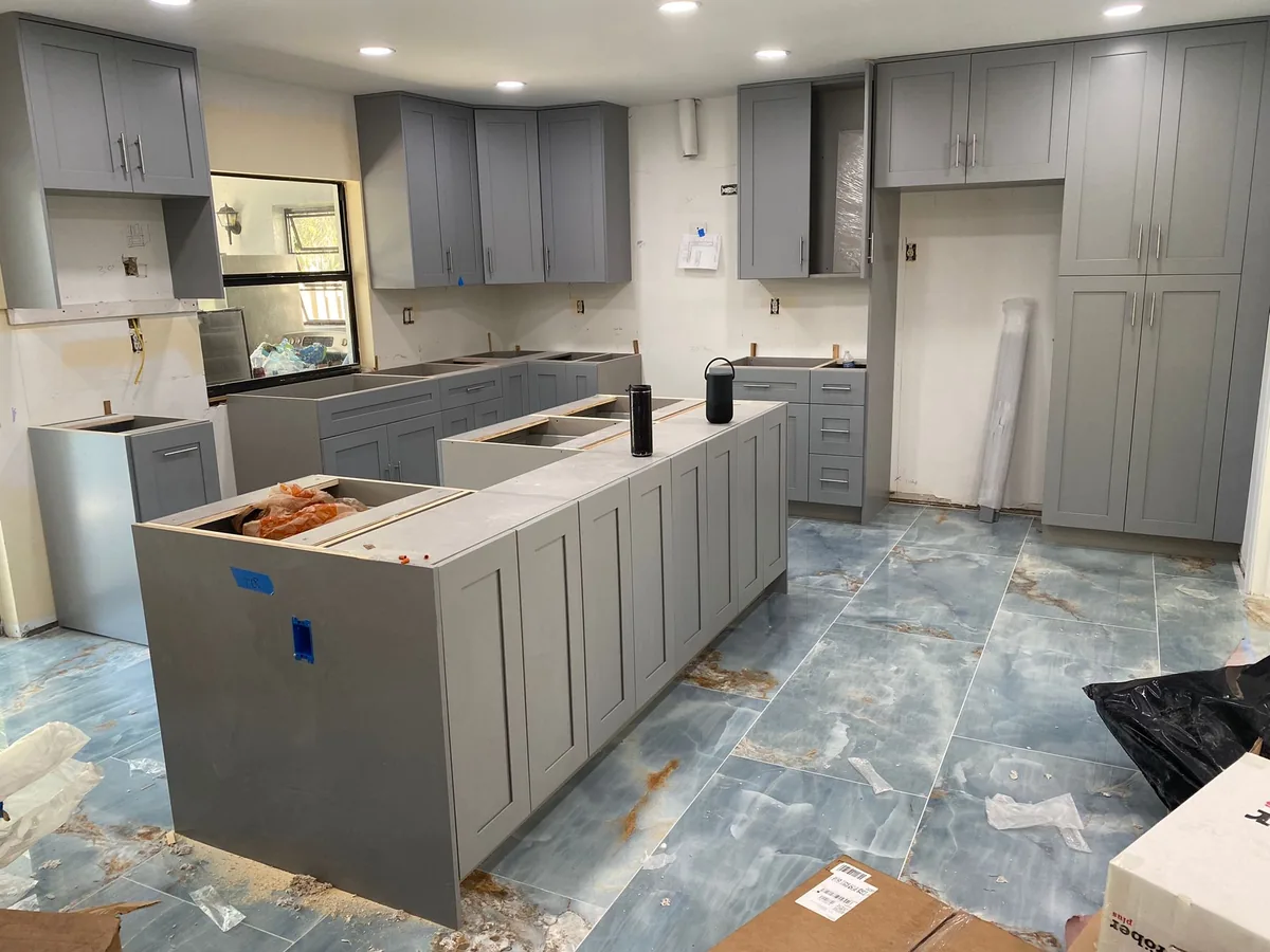 Gray shaker cabinets and island being installed over blue tile floor