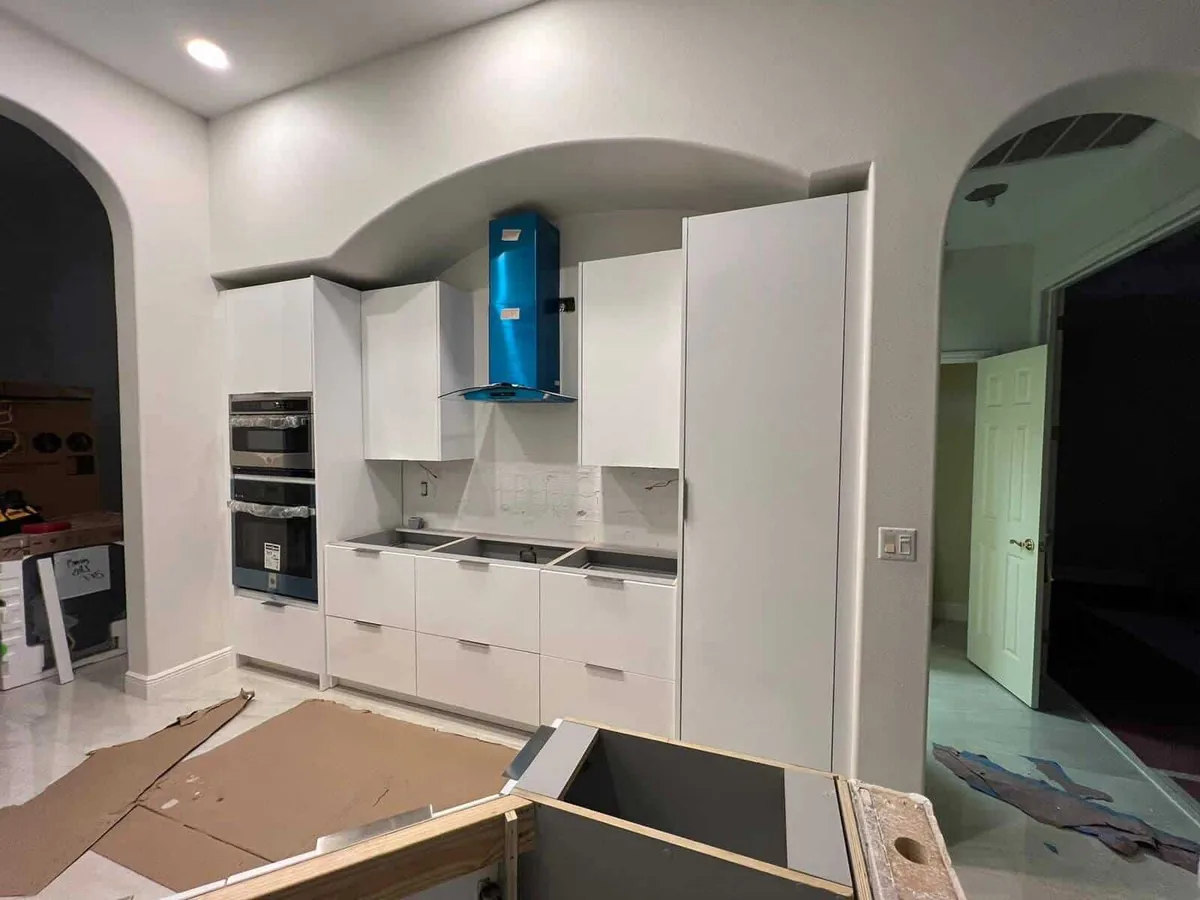 White slab cabinets and blue hood fitted under an arch, in progress