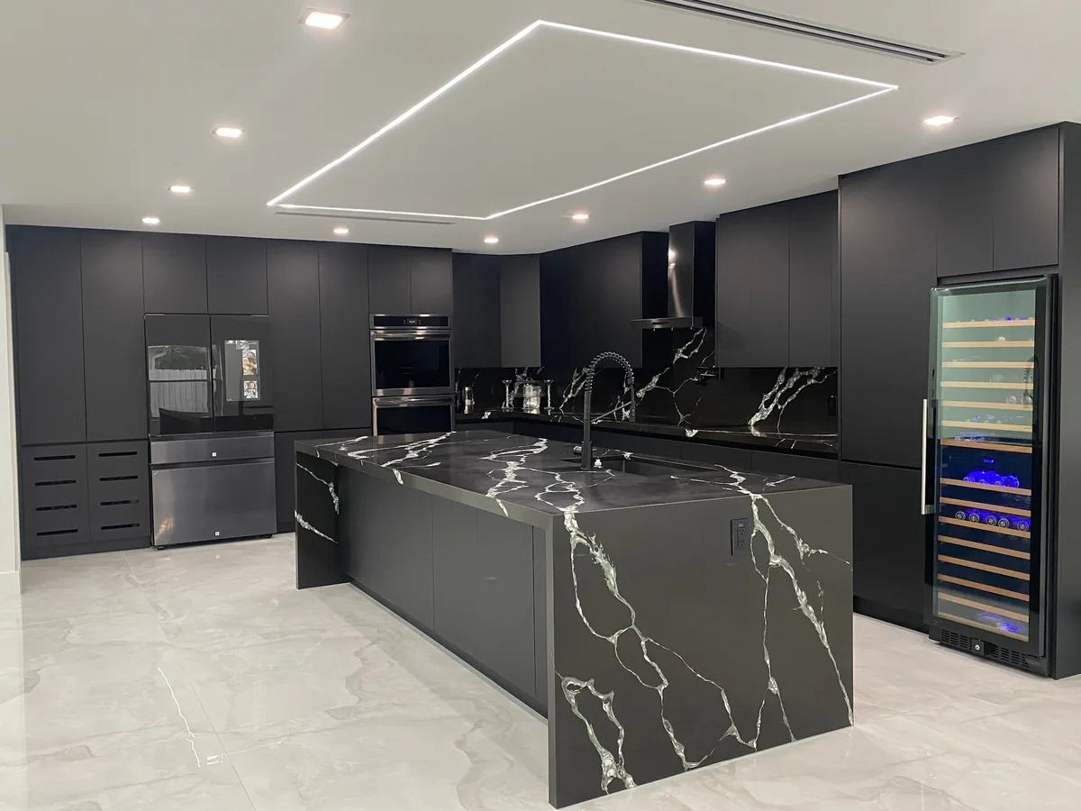 Charcoal flat panel kitchen with a black and white veined waterfall quartz island and a recessed LED light frame in the ceiling