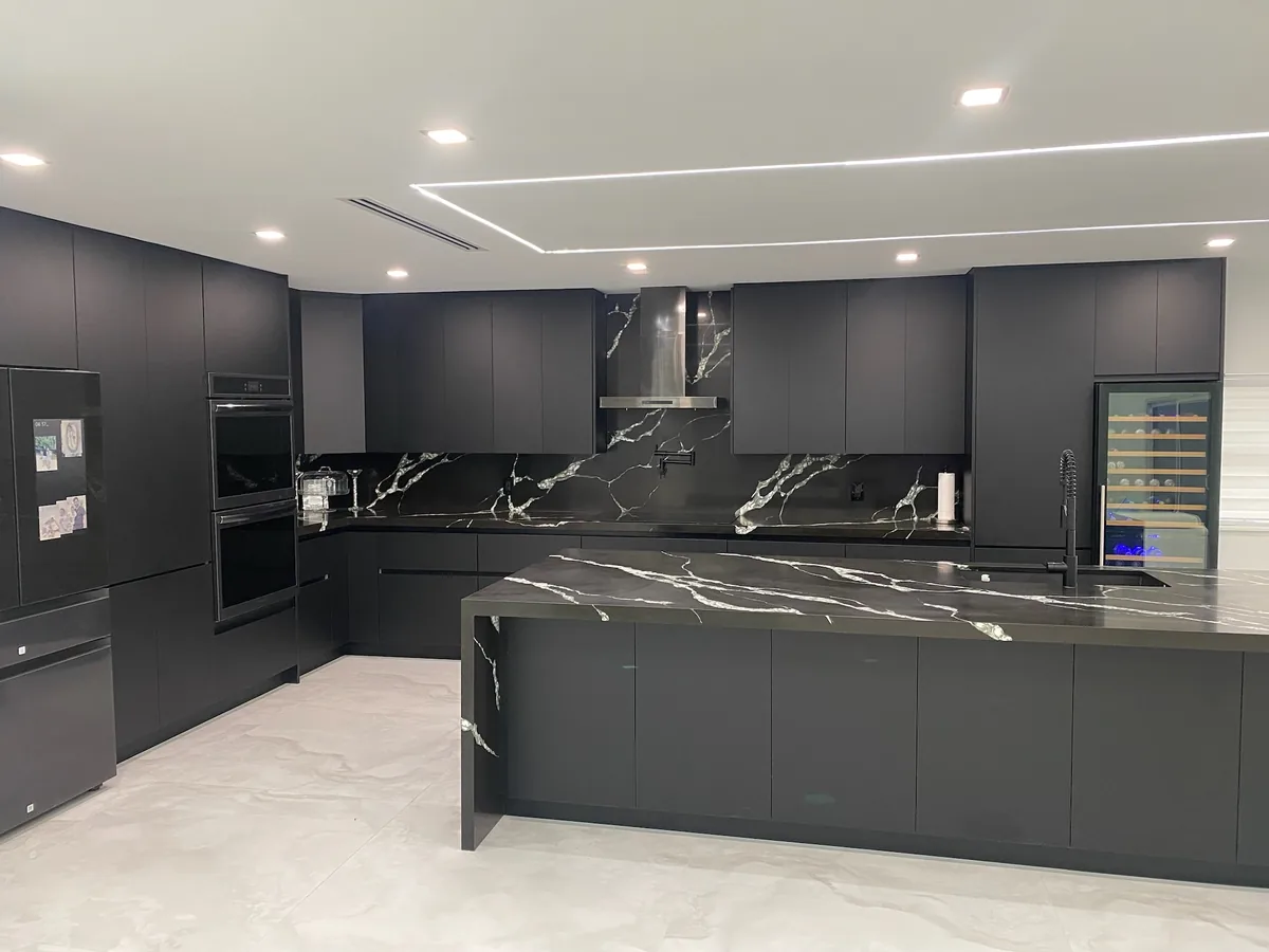 Wide view of a charcoal handleless kitchen with black veined quartz island and backsplash under linear ceiling lighting