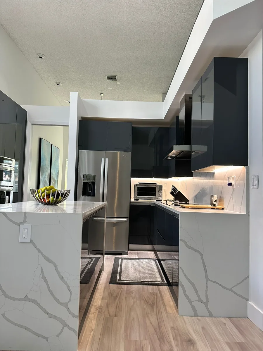 Dark gloss kitchen cabinets with a white veined quartz waterfall peninsula and wood look floor