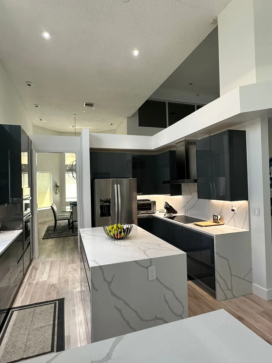 Kitchen with dark gloss cabinets, stainless refrigerator and white quartz waterfall island under a dropped soffit