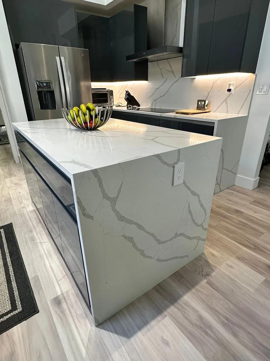White quartz waterfall island edge with dark gloss base cabinets and stainless refrigerator