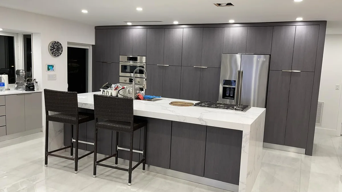 Dark flat panel kitchen with a white quartz island, bar stools and wall ovens
