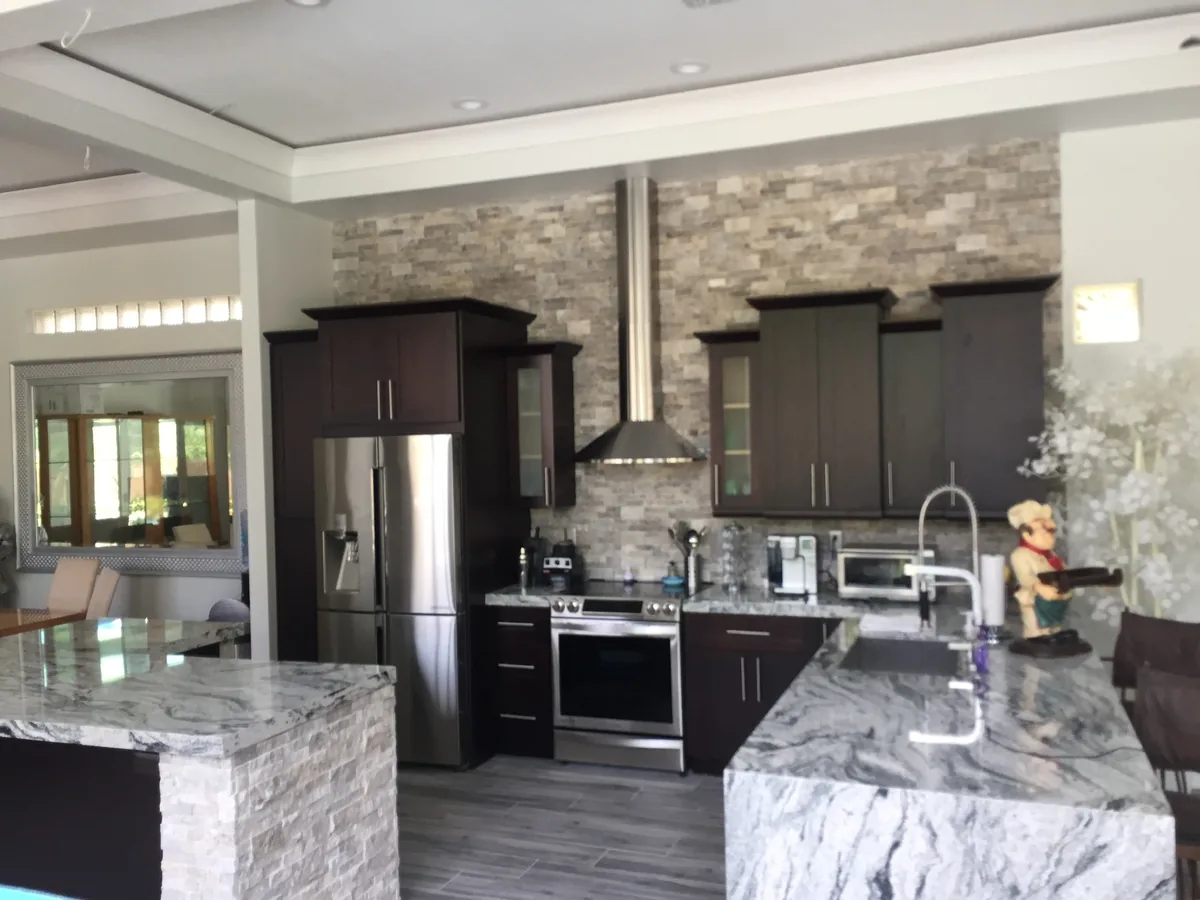 Espresso cabinets with a stacked stone backsplash and gray swirl granite waterfall island