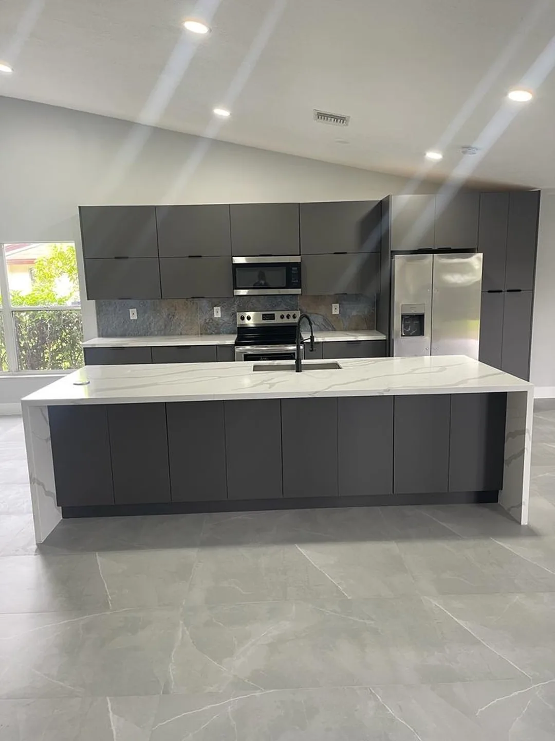 Gray flat panel kitchen with a long white quartz island and large format tile