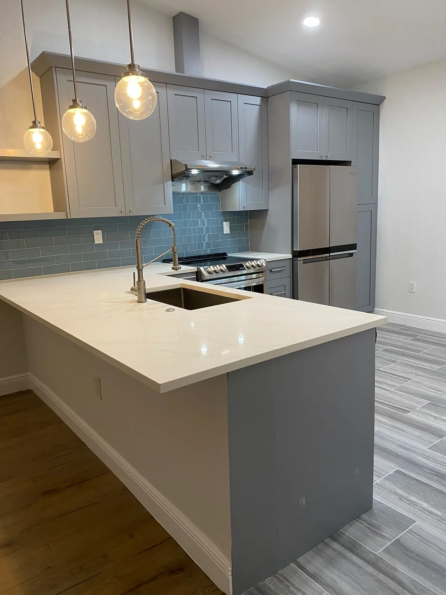 Gray shaker kitchen with a blue glass subway backsplash and white quartz peninsula