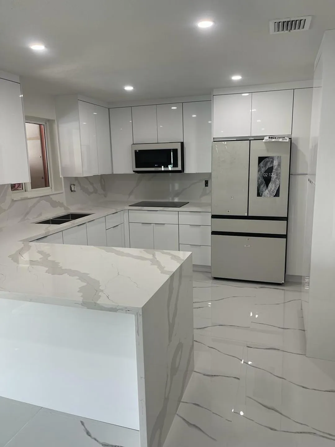 White gloss kitchen with marble look quartz waterfall peninsula and porcelain floor