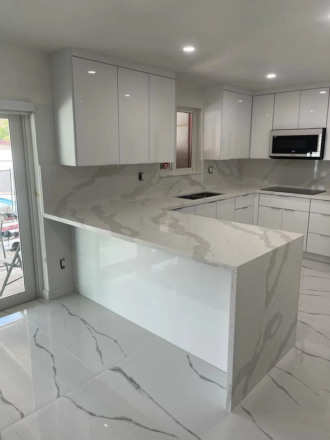 White gloss cabinets with a marble look quartz waterfall peninsula