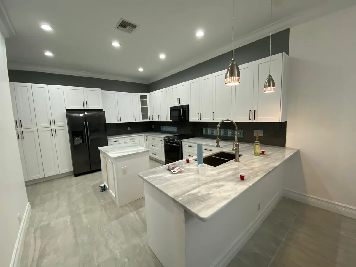 White shaker kitchen with a marble look quartz peninsula, glass pendants and black appliances