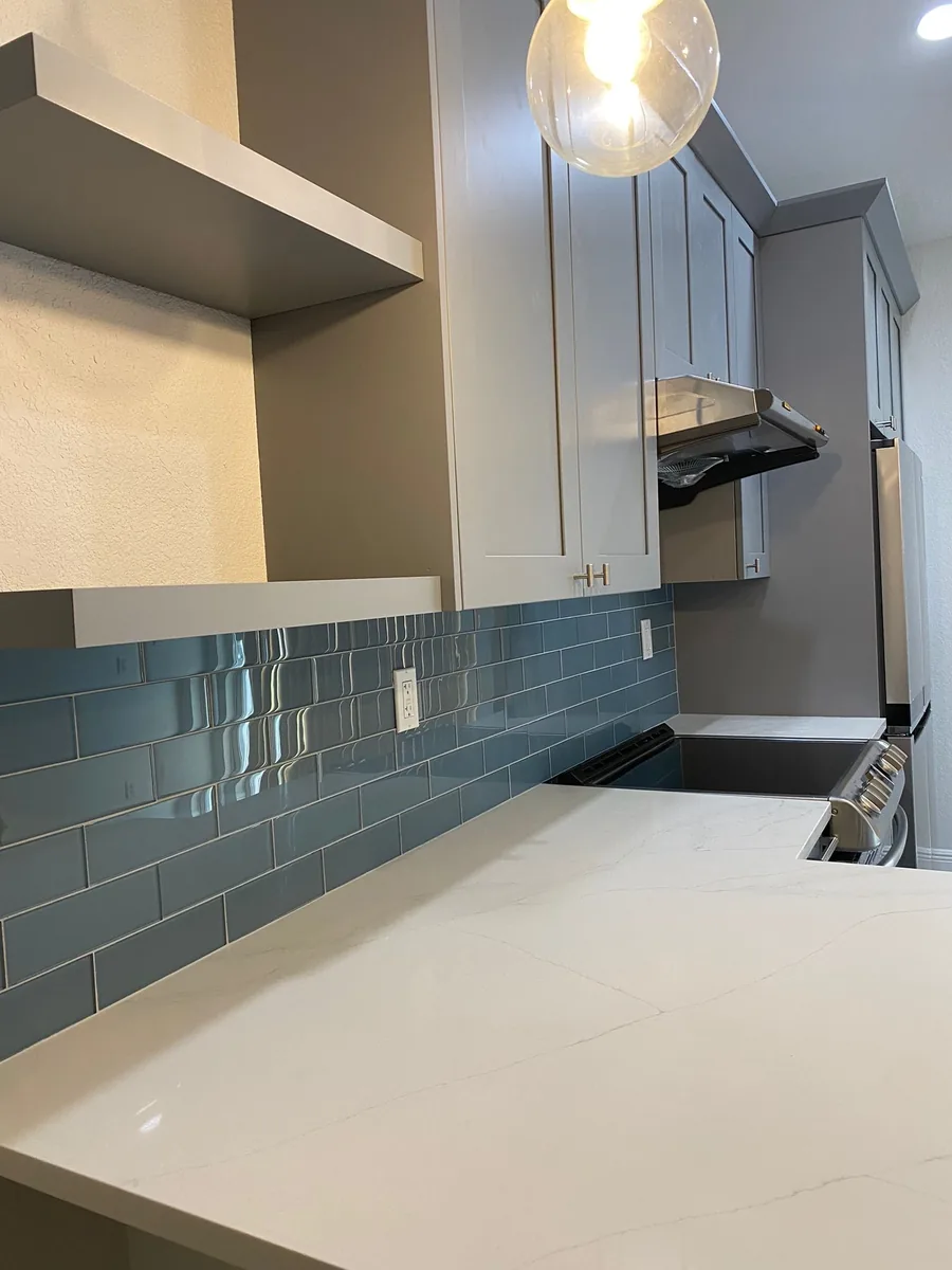 White quartz countertop with a blue glass subway tile backsplash and range hood