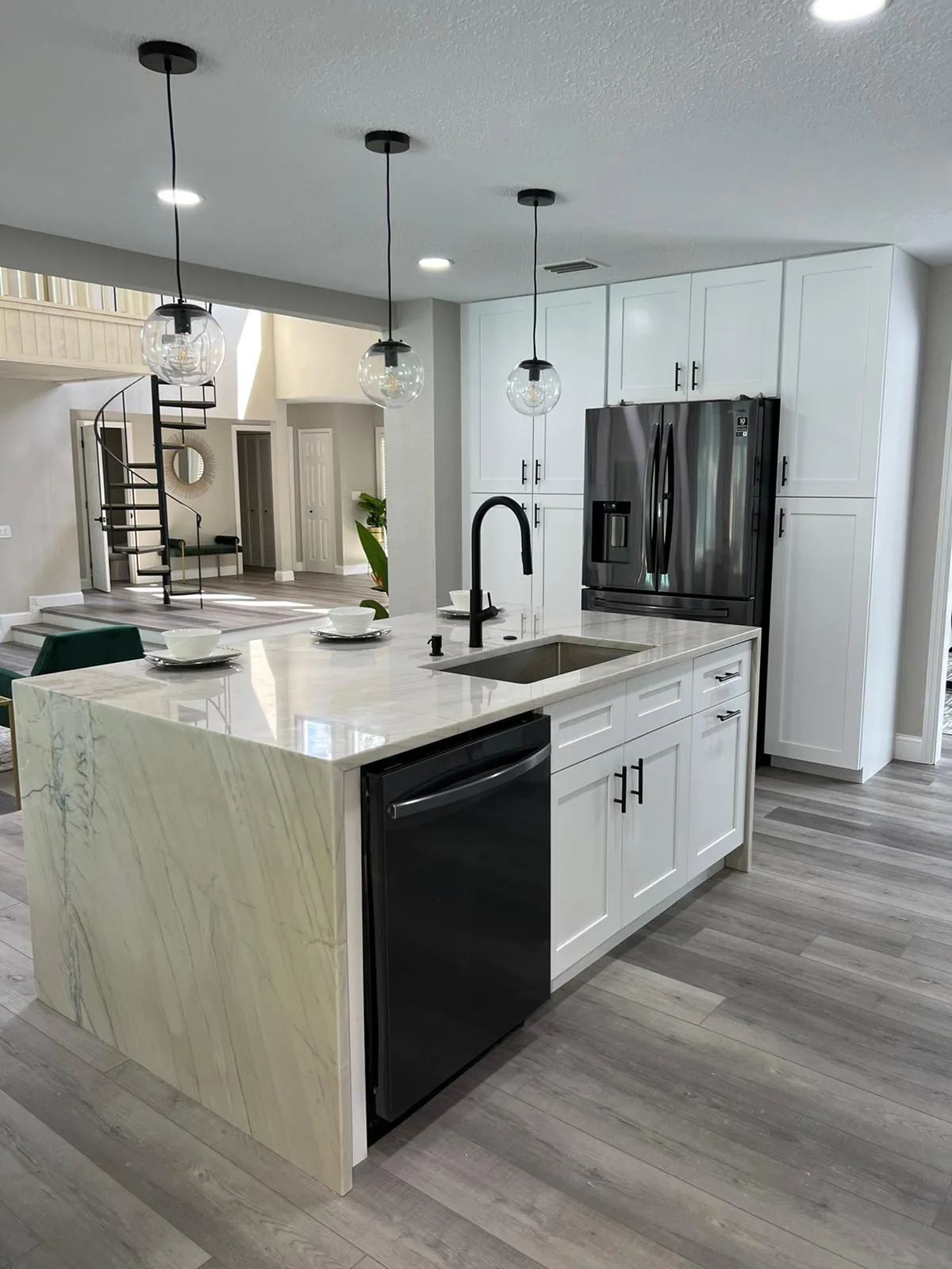 Quartzite waterfall island with black pendant lights in a white shaker kitchen