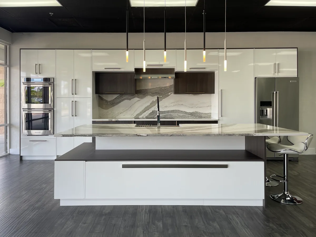 Showroom kitchen display with white gloss cabinets and a marble look backsplash