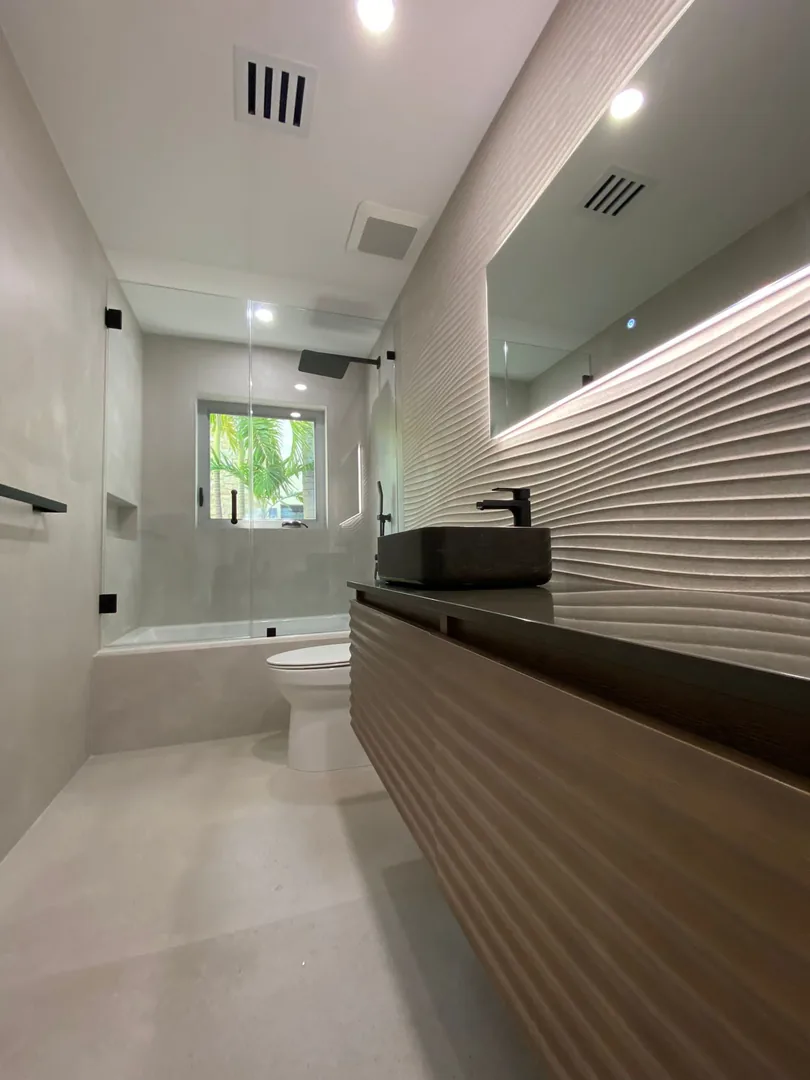 Fluted wood vanity with a black vessel sink and LED lit wall